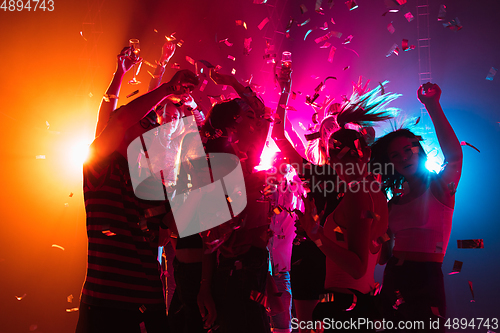 Image of A crowd of people in silhouette raises their hands on dancefloor on neon light background