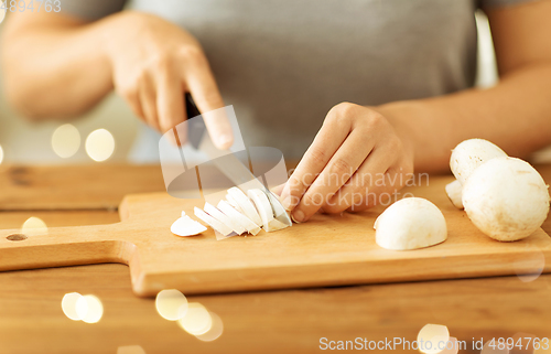 Image of woman cutting champignons by knife on board