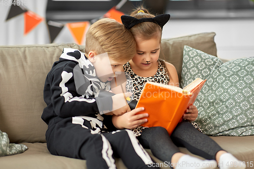 Image of kids in halloween costumes reading book at home