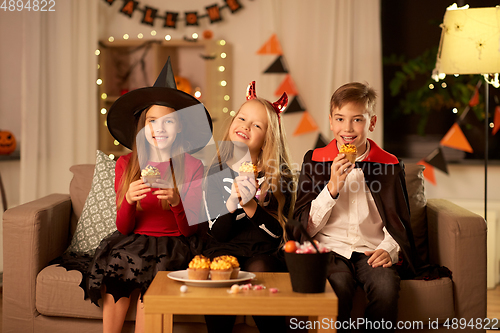 Image of kids in halloween costumes eating cupcakes at home