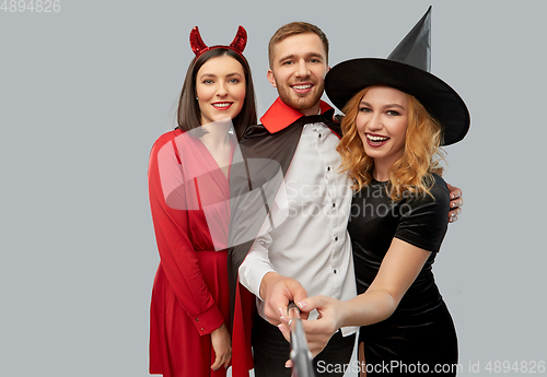 Image of happy friends in halloween costumes taking selfie