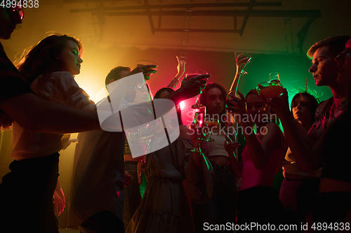 Image of A crowd of people in silhouette raises their hands on dancefloor on neon light background