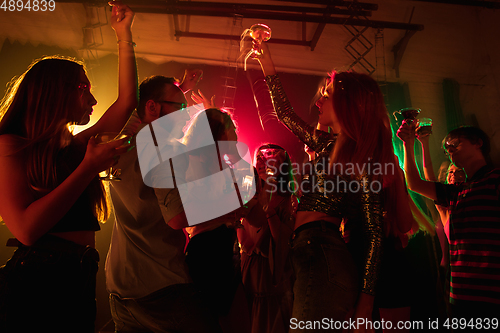 Image of A crowd of people in silhouette raises their hands on dancefloor on neon light background