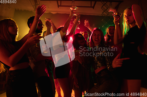 Image of A crowd of people in silhouette raises their hands on dancefloor on neon light background