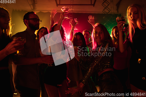 Image of A crowd of people in silhouette raises their hands on dancefloor on neon light background