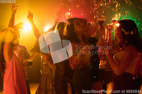 Image of A crowd of people in silhouette raises their hands on dancefloor on neon light background