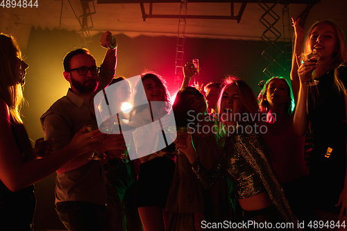 Image of A crowd of people in silhouette raises their hands on dancefloor on neon light background