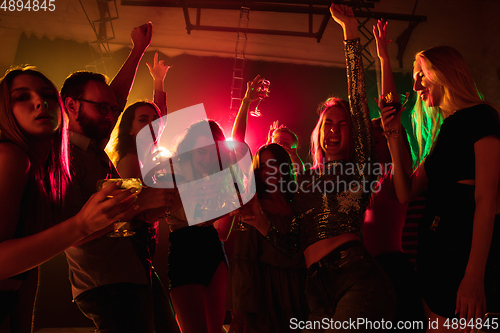 Image of A crowd of people in silhouette raises their hands on dancefloor on neon light background