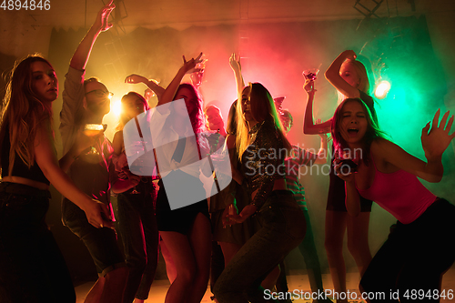 Image of A crowd of people in silhouette raises their hands on dancefloor on neon light background