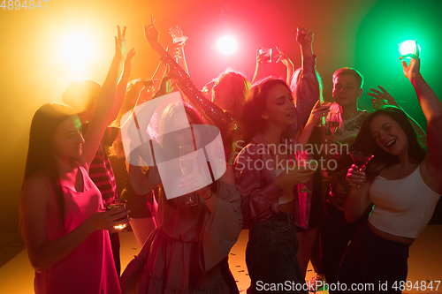 Image of A crowd of people in silhouette raises their hands on dancefloor on neon light background