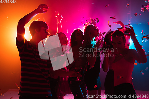 Image of A crowd of people in silhouette raises their hands on dancefloor on neon light background