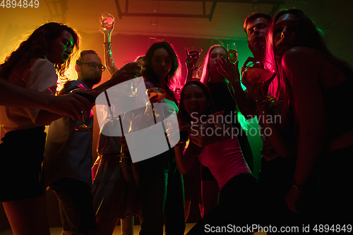 Image of A crowd of people in silhouette raises their hands on dancefloor on neon light background