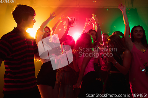 Image of A crowd of people in silhouette raises their hands on dancefloor on neon light background