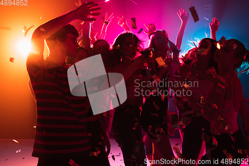 Image of A crowd of people in silhouette raises their hands on dancefloor on neon light background