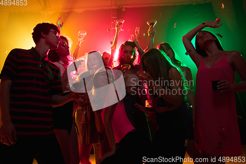 Image of A crowd of people in silhouette raises their hands on dancefloor on neon light background