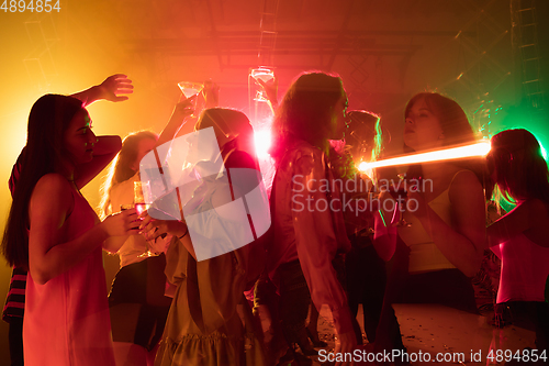 Image of A crowd of people in silhouette raises their hands on dancefloor on neon light background