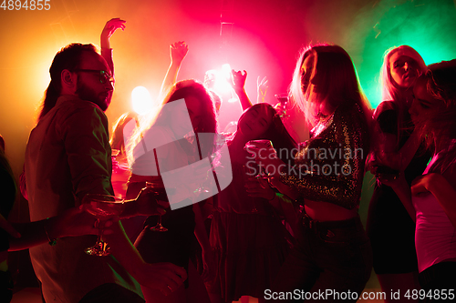 Image of A crowd of people in silhouette raises their hands on dancefloor on neon light background