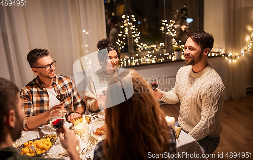 Image of happy friends drinking red wine at christmas party