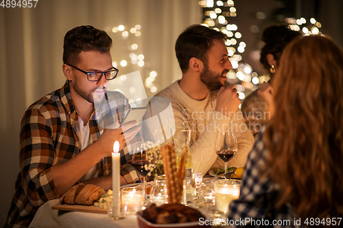 Image of man with smartphone at dinner party with friends