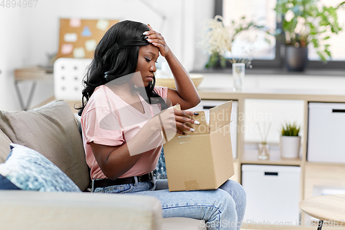 Image of sad african american woman with parcel box at home