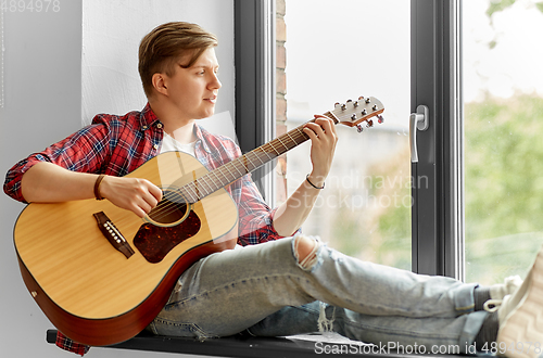 Image of young man playing guitar sitting on windowsill