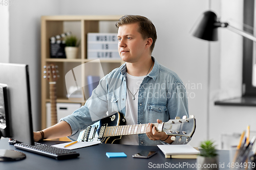 Image of young man with computer playing guitar at home