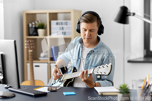 Image of man in headphones playing bass guitar at home