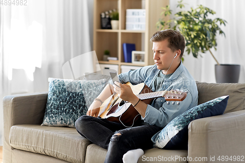 Image of man with guitar, earphones and smartphone at home