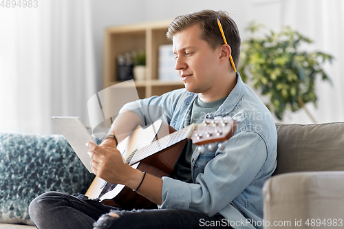 Image of young man with guitar and music book at home