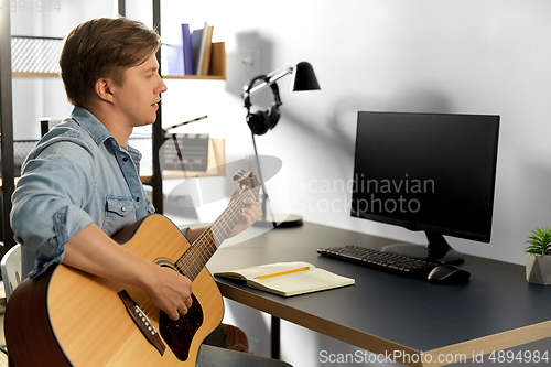 Image of young man with computer playing guitar at home