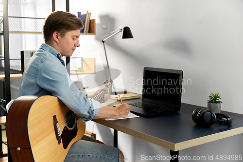 Image of man with guitar writing to music book at home