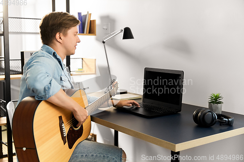 Image of young man with laptop and guitar at home