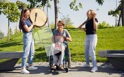 Image of Happy handicapped man on a wheelchair spending time with friends playing live instrumental music outdoors