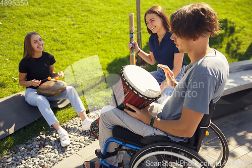 Image of Happy handicapped man on a wheelchair spending time with friends playing live instrumental music outdoors
