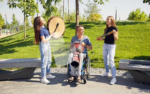 Image of Happy handicapped man on a wheelchair spending time with friends playing live instrumental music outdoors