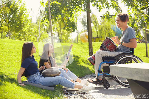 Image of Happy handicapped man on a wheelchair spending time with friends playing live instrumental music outdoors