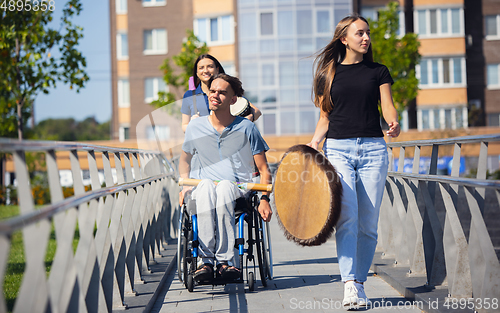 Image of Happy handicapped man on a wheelchair spending time with friends playing live instrumental music outdoors