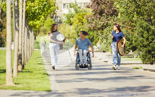 Image of Happy handicapped man on a wheelchair spending time with friends playing live instrumental music outdoors