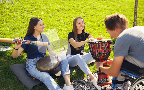 Image of Happy handicapped man on a wheelchair spending time with friends playing live instrumental music outdoors