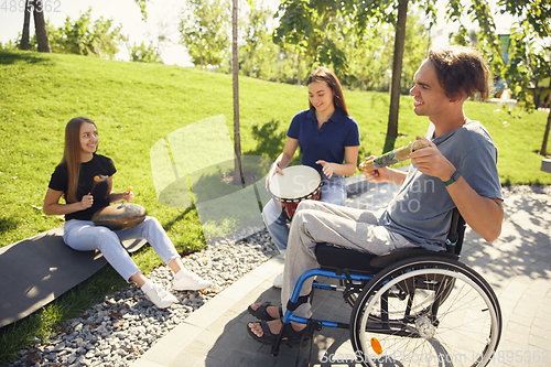 Image of Happy handicapped man on a wheelchair spending time with friends playing live instrumental music outdoors