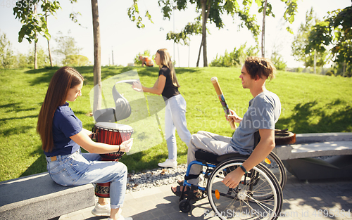 Image of Happy handicapped man on a wheelchair spending time with friends playing live instrumental music outdoors