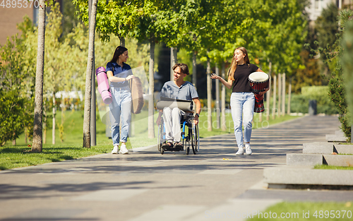 Image of Happy handicapped man on a wheelchair spending time with friends playing live instrumental music outdoors