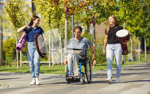 Image of Happy handicapped man on a wheelchair spending time with friends playing live instrumental music outdoors