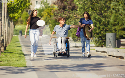 Image of Happy handicapped man on a wheelchair spending time with friends playing live instrumental music outdoors