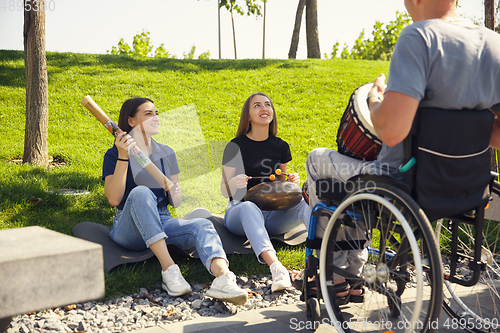 Image of Happy handicapped man on a wheelchair spending time with friends playing live instrumental music outdoors