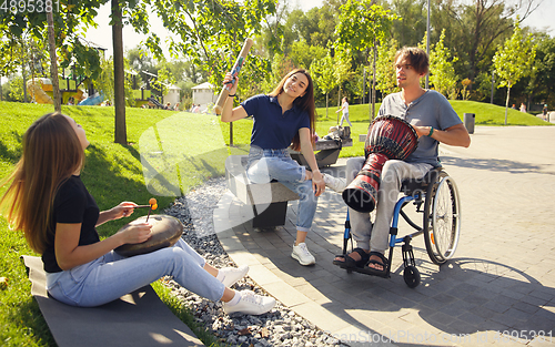 Image of Happy handicapped man on a wheelchair spending time with friends playing live instrumental music outdoors