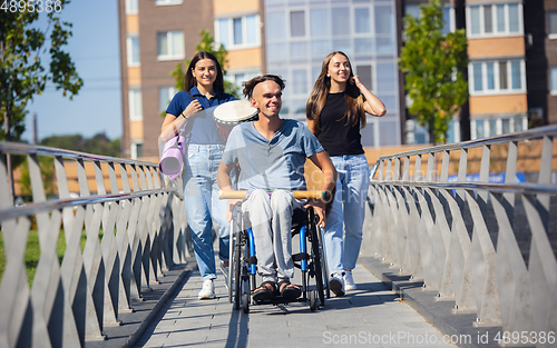 Image of Happy handicapped man on a wheelchair spending time with friends playing live instrumental music outdoors