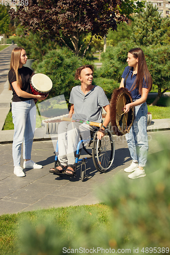 Image of Happy handicapped man on a wheelchair spending time with friends playing live instrumental music outdoors