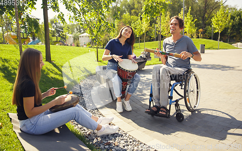 Image of Happy handicapped man on a wheelchair spending time with friends playing live instrumental music outdoors