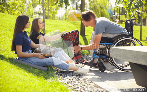 Image of Happy handicapped man on a wheelchair spending time with friends playing live instrumental music outdoors